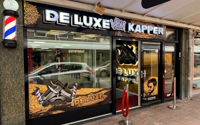 De gevel met lichtletters, barberpaal en de rode loper met chromen paaltjes