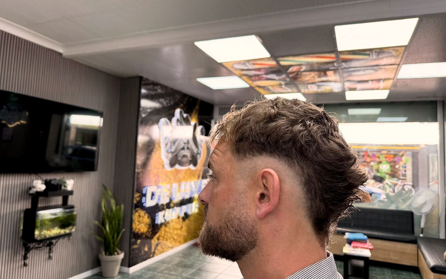 Fade met krullen in de zaak, met de verlichte goudwand en het embleem van De Luxe Kapper op de achtergrond